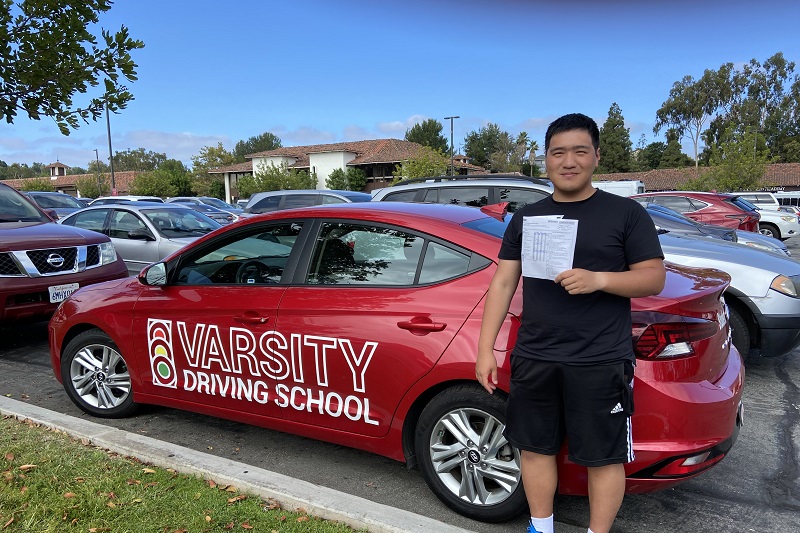 Driving School for Behind the Wheel Training in California Student Standing Next to a Training Vehicle in a Parking Lot