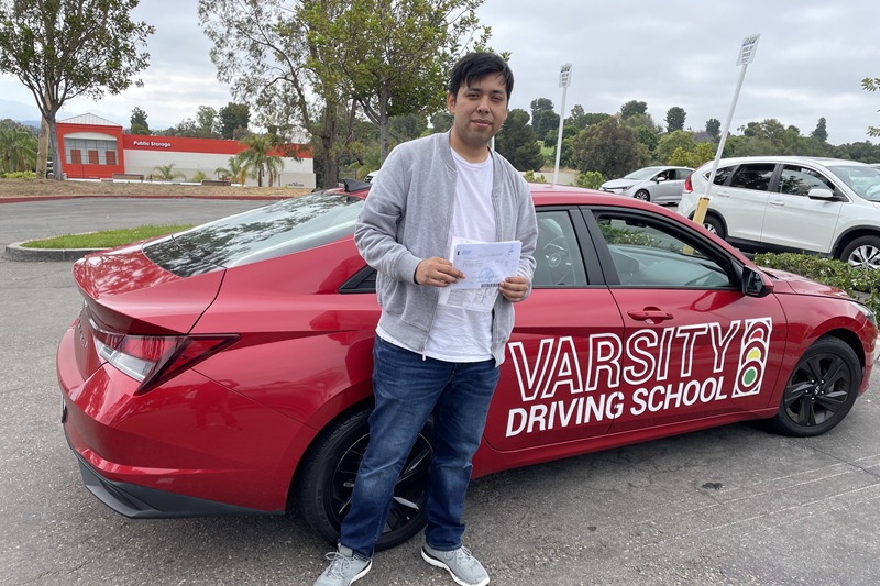 Best John F. Kennedy High School Driving School Student Standing Next to a Training Vehicle in a Parking Lot